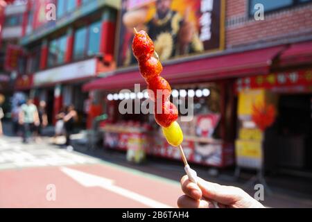 Hand holding a traditional Chinese snack, candied strawberries fruit skewers Stock Photo