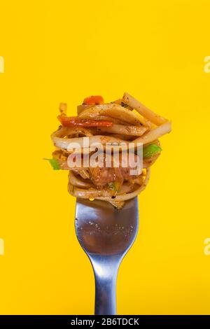 Classic spaghetti carbonara with chicken wound on fork on vivid yellow background. Eating spaghetti requires fork. Italian pasta and fast food takeawa Stock Photo