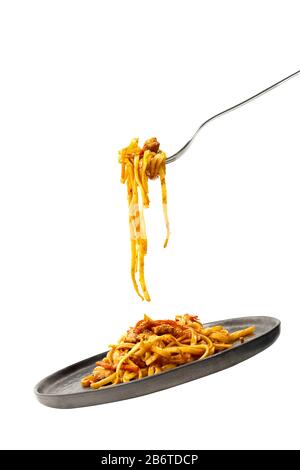 Pasta flying with fork and black plate. Isolated on white background. Illusions of levitation and falling. Classic pasta recipe. Stock Photo