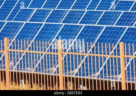 Security fence prevents unauthorised access to solar power electric generating system and facility. Dusty solar panels surface requires maintenance an Stock Photo