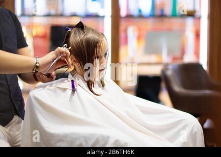 Child getting haircut in beauty salon. Hairdresser cutting hair. Little girl with dark blond shoulder length bob at stylist. Kids spa. Style and fashi Stock Photo