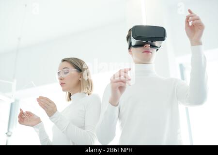 Young man in VR goggles testing new virtual reality app while young woman checking it on futuristic tablet Stock Photo
