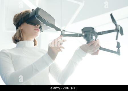 Below view of young woman in white turtleneck synchronizing drone with virtual reality goggles Stock Photo