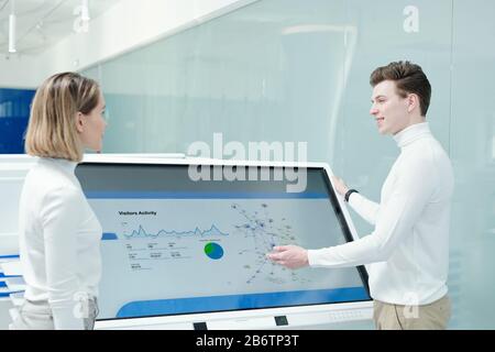 Smiling young male consultant explaining scheme to customer while presenting product using interactive display Stock Photo