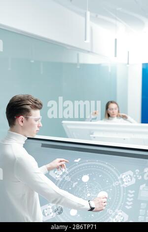 Over shoulder view of young man in smart goggles composing elements on scheme using interactive display in modern office Stock Photo