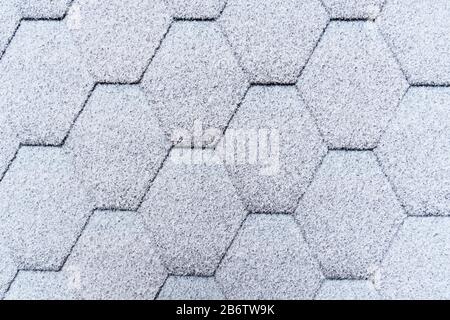 Asphalt roofing shingles texture covered with light snow. House roof shingles covered with frost. Snow covered roof of the house. Stock Photo