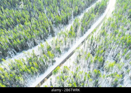 Aerial view of a winter country road in the forest with moving cars. Beautiful landscape. Captured from above with a drone. Aerial bird's eye road wit Stock Photo