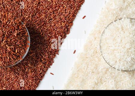 Raw red and white rice grains in a transparent glass plate. Rice grains scattered on a white background. Problem of choice. Closeup, top view Stock Photo