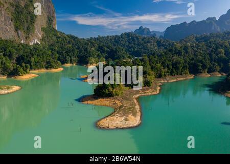 Aerial view of tiny fingers of tropical rainforest extending into a huge lake surrounded by towering limestone cliffs (Khao Sok) Stock Photo