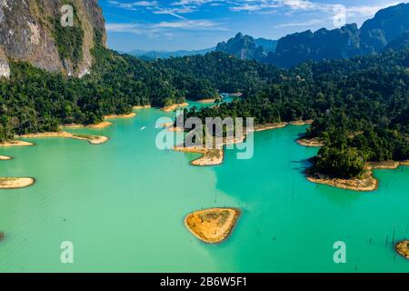 Aerial drone view looking down onto tiny, jungle covered islands in a huge lake surrounded by limestone cliffs. (Cheow Lan Lake, Khao Sok) Stock Photo