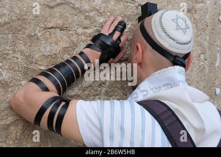 A Jewish man wrapped with traditional religious Talit shawl and Tefillin phylacteries praying in the Western Wall or Kotel old city East Jerusalem Israel Stock Photo