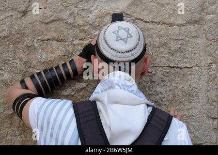 A Jewish man wrapped with traditional religious Talit shawl and Tefillin phylacteries praying in the Western Wall or Kotel old city East Jerusalem Israel Stock Photo