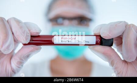 Healthcare to aid recovery from COVID-19. Scientist wear surgical gloves and mask with a coronavirus infected blood sample test. Asian woman doctor bi Stock Photo