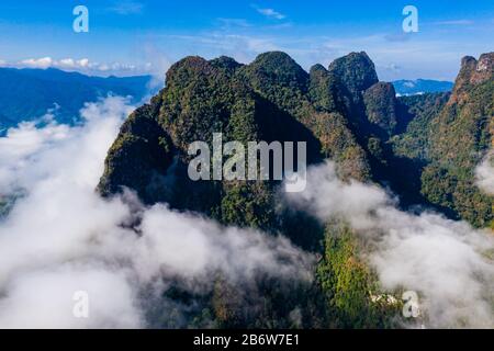 Aerial view of clouds and mist drifting next to towering, jungle covered limestone mountains Stock Photo