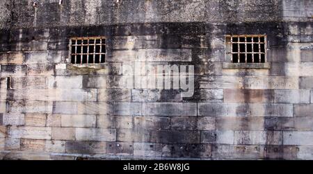 Historical sandstone convict built brick prison building, windows rusting security grill, wall background Stock Photo