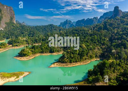 Aerial view of tiny fingers of tropical rainforest extending into a huge lake surrounded by towering limestone cliffs (Khao Sok) Stock Photo