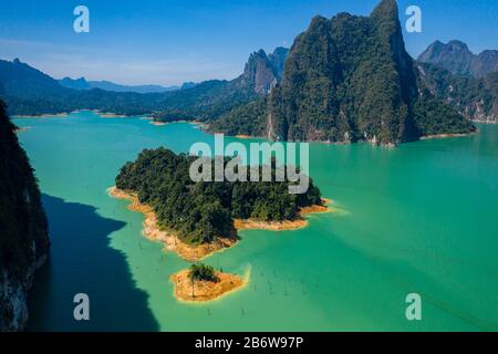 Aerial drone view looking down onto tiny, jungle covered islands in a huge lake surrounded by limestone cliffs. (Cheow Lan Lake, Khao Sok) Stock Photo