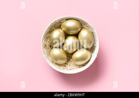 Easter golden chicken eggs in white bowl on pink background. View from above. Minimal concept. Stock Photo