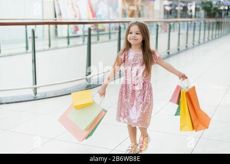 Cheerful preschool girl walking with shopping bags. Pretty smiling little girl with shopping bags posing in the shop. The concept of shopping in stores. Stock Photo