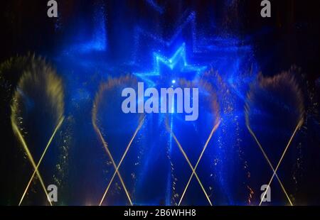 Colorful water fountains. Beautiful laser and fountains show. Large multi colored decorative dancing water jet led light fountain show at night. Dark Stock Photo