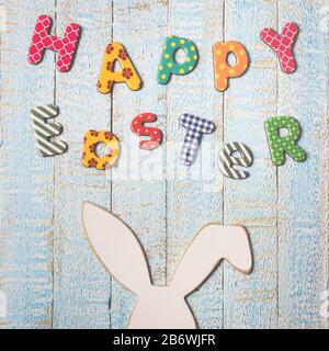 Easter composition with with Easter bunny and text happy Easter on light blue wooden background. Top view with copy space. Stock Photo