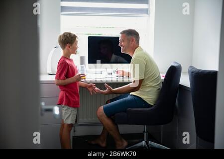 A side-view shot of a father and son sitting down using a computer, they are learning together. Stock Photo