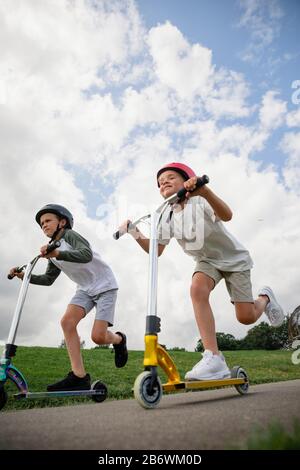 A low angle view shot of two young boys playing together on push scooters. Stock Photo