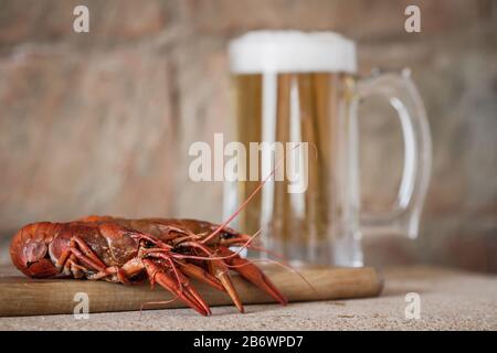 Boiled red crawfish on the wooden surface against a mug of beer background. Closeup, selective focus, toned, brick brown background Stock Photo