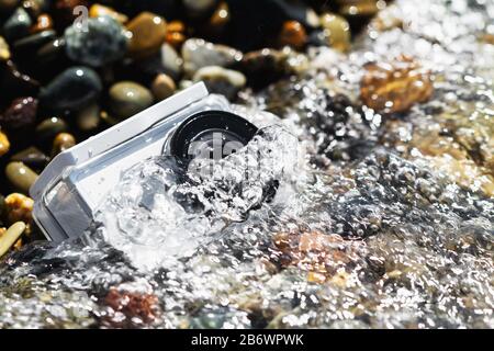 White action camera with underwater case in water on the pebble beach Stock Photo
