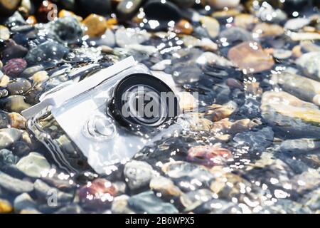 White action camera with underwater case in water on the pebble beach Stock Photo