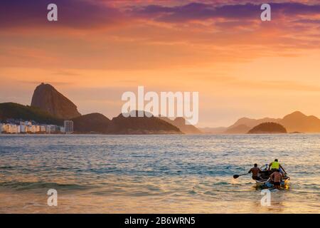 Brazil, Rio, Rio de Janeiro. Fishermen launching a boat with the Sugar Loaf, Leme hill and the mountains of Rio de Janeiro behind Stock Photo