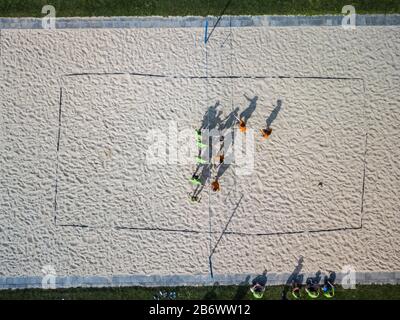 Aerial view of a beach volleyball  pitch with people getting ready for a game in warm morning sun, casting long shadows Stock Photo