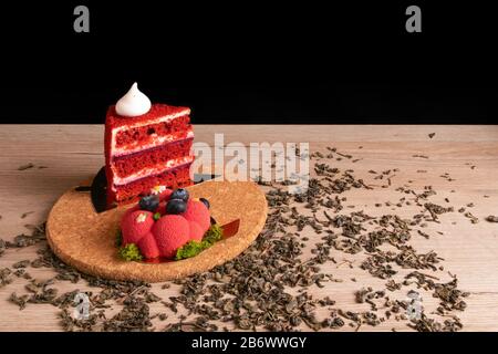 Two appetizing delicious red cakes on a cork stand with scattered dry green tea Stock Photo