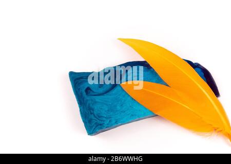 Thin flat piece of blue mint handmade soap and two orange feathers isolated on white background Stock Photo