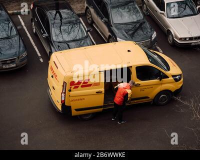 Moscow, Russia - March 11, 2020: DHL Deutsche Post courier in yellow-red uniform near minivan with company logos. DHL International GmbH is world larg Stock Photo