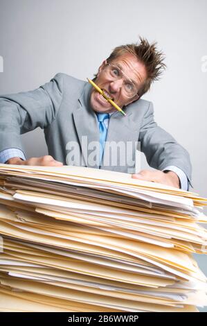 Overworked office worker with pencil in his mouth trying to lift a heavy stack of documents on his desk Stock Photo