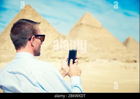 Businessman using his smartphone in desert sun against background of the Great Pyramids in Egypt Stock Photo