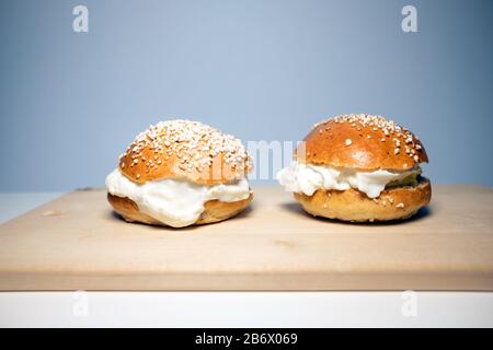 A traditional Scandinavian shrovetide buns with whipped cream on white table. Shrovetide buns are classic delicacies for Shorevetide Sunday & Tuesday. Stock Photo