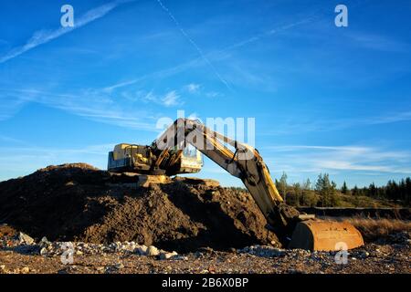 Yellow excavator on a road construction site against blue sky. Stock Photo
