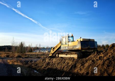 Yellow excavator on a road construction site against blue sky. Stock Photo
