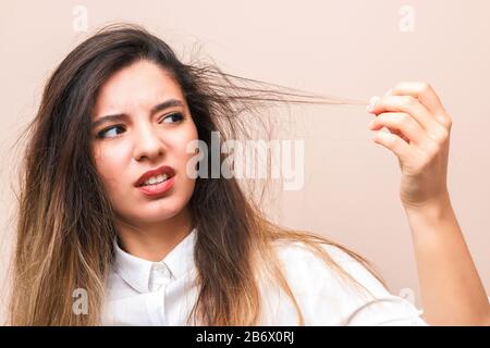 hair problems. young woman in white shirt checking her britle, damaged, and split hairs against pink background Stock Photo