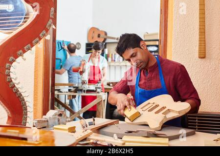 Young apprentice works on a guitar in the workshop of the guitar maker Stock Photo