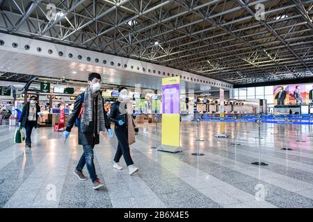 Milan Malpensa Airport, Italy. 12th Mar, 2020. Passengers wearing protective face masks in the empty departures terminal of Malpensa (MXP) airport. US President Trump suspended travel from Europe (except UK) for 30 days amid Coronavirus outbreak fears. Credit: Piero Cruciatti/Alamy Live News Stock Photo