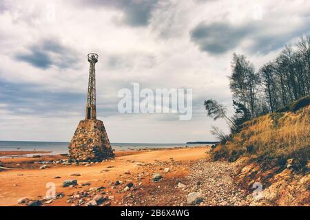 Old ruined lighthouse on the beach of the Baltic Sea by the sand dunes with trees Stock Photo
