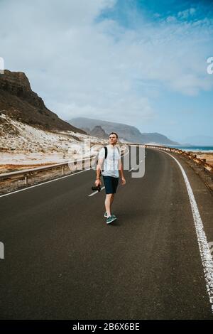 Traveler walks in the center of an epic winding road. Huge volcanic mountains in the distance behind him. Sao Vicente Cape Verde. Stock Photo