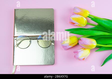 Colorful pinc and yellow tulip with notebook and eyeglasses flat lay isolated on pinc background top view. Spring flower. Womans day, mothers day Stock Photo