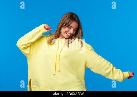 Relaxed and carefree happy blond girl having fun, dancing to music, enjoying leisure with friends at awesome party or concert, move hands sideways Stock Photo