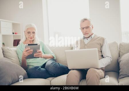 Photo of interested grandma using electronic gadget enjoying fresh news on site and smart granddad wearing specs typing e-mail to friends they are Stock Photo
