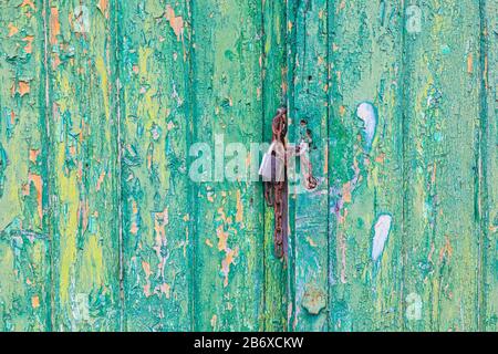 Rusty lock and chain holding weathered doors with flaking yellow and green paint closed. Stock Photo