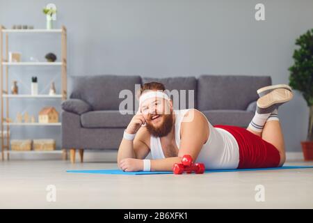 Funny red fat man doing exercises on the floor smiling while lying on the floor at home. Stock Photo